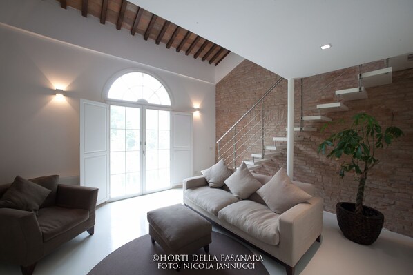 Una sala moderna con sofá, sillón y una escalera frente a una pared de ladrillo.