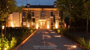 A stone house with a central entrance, surrounded by a garden and a gravel path leading to the door. - Villa Horti della Fasanara (Ferrara)