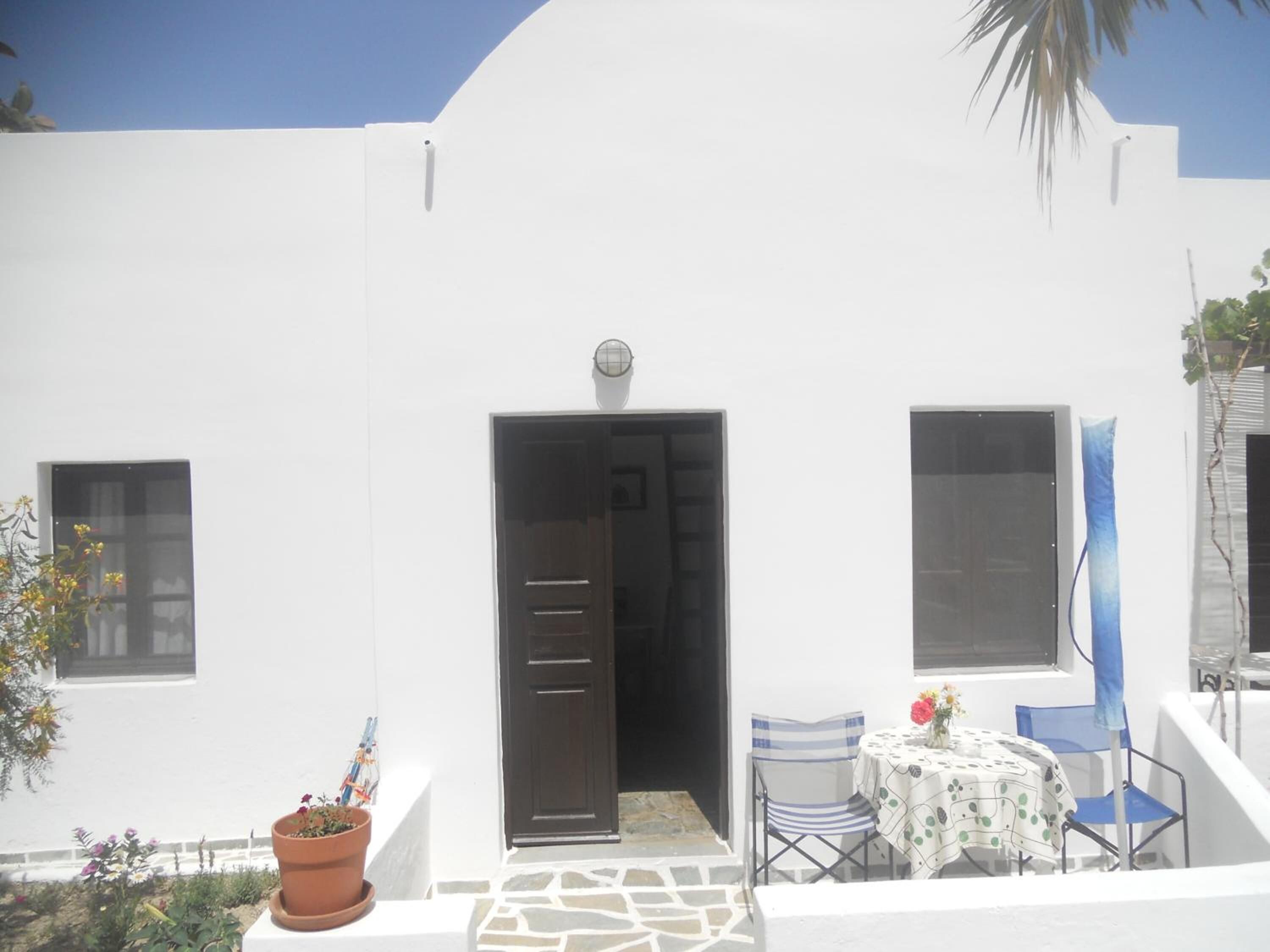 A white building with a door, windows, and a small patio area with a table and chairs.