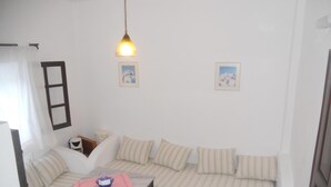 A compact living space with a sofa, a small table, and a hanging light fixture. - Villa Ostria (Santorini)