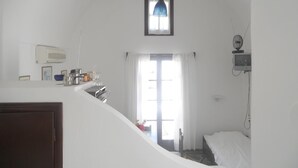 A compact, well-lit room with a kitchenette, a bed, and a small window. - Villa Ostria (Santorini)