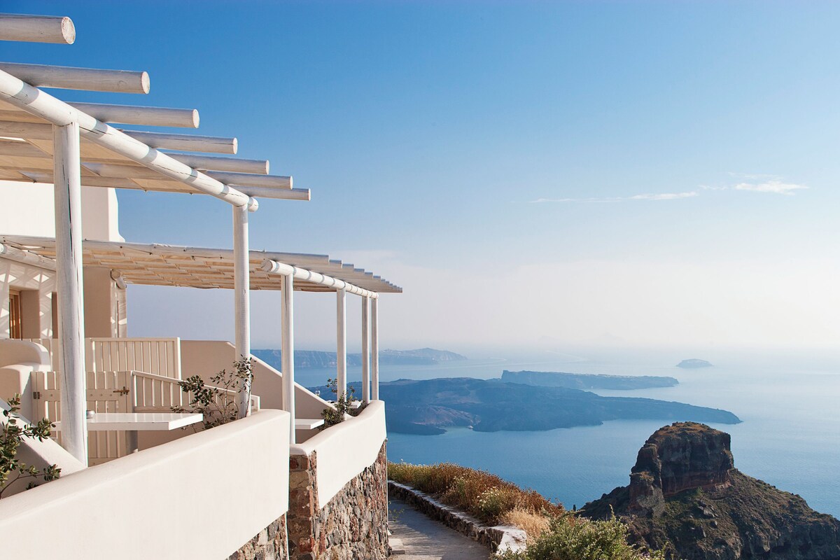 A coastal hotel with a terrace overlooking the sea, featuring a stone pathway and a pergola.
