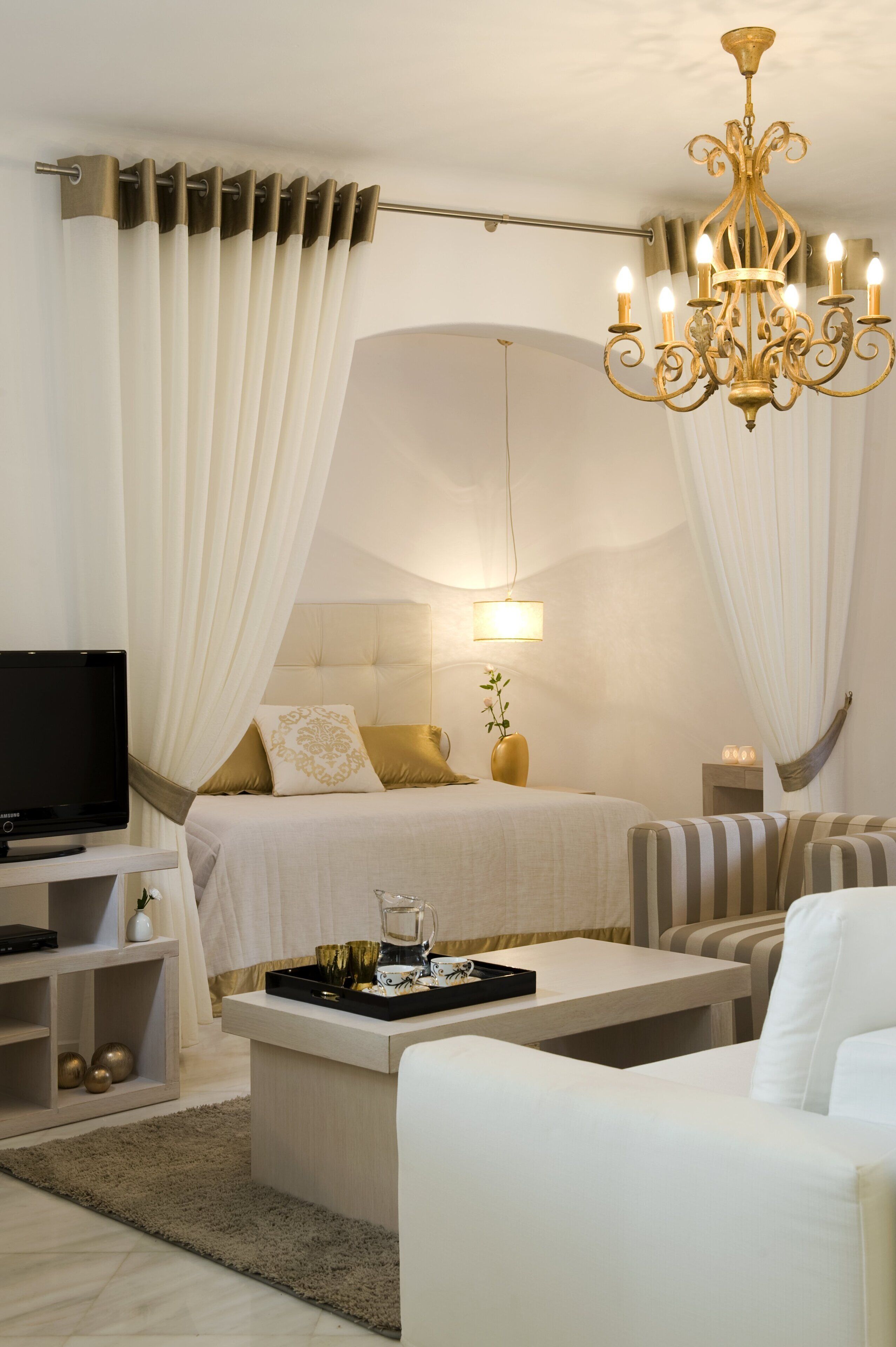 A modern bedroom with a large bed, a television, a bedside table, and a chandelier.