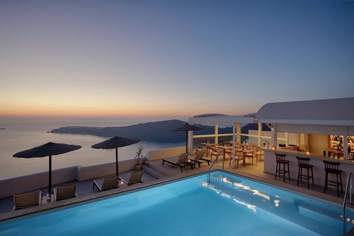 A poolside area with lounge chairs and umbrellas, overlooking a body of water at sunset.