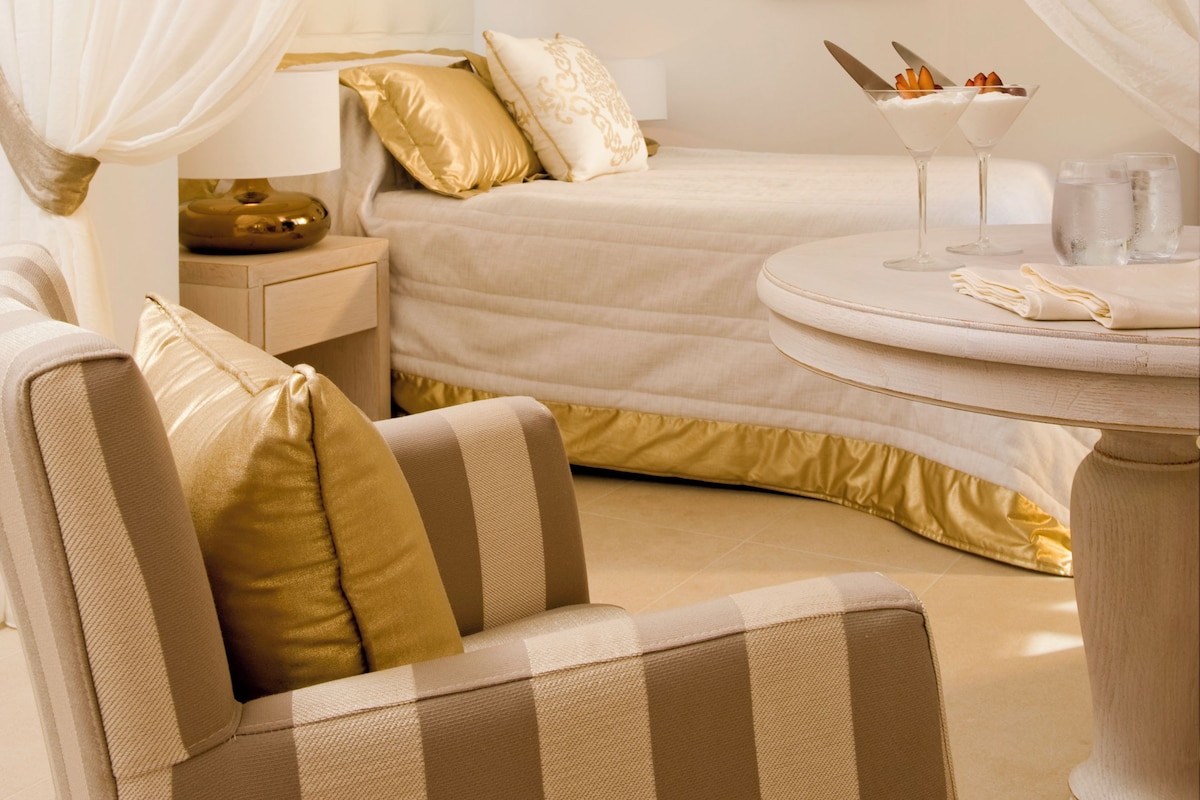 Una habitación de hotel con una cama, una mesita de noche, una silla y una pequeña mesa con un vaso de agua y un plato de comida.