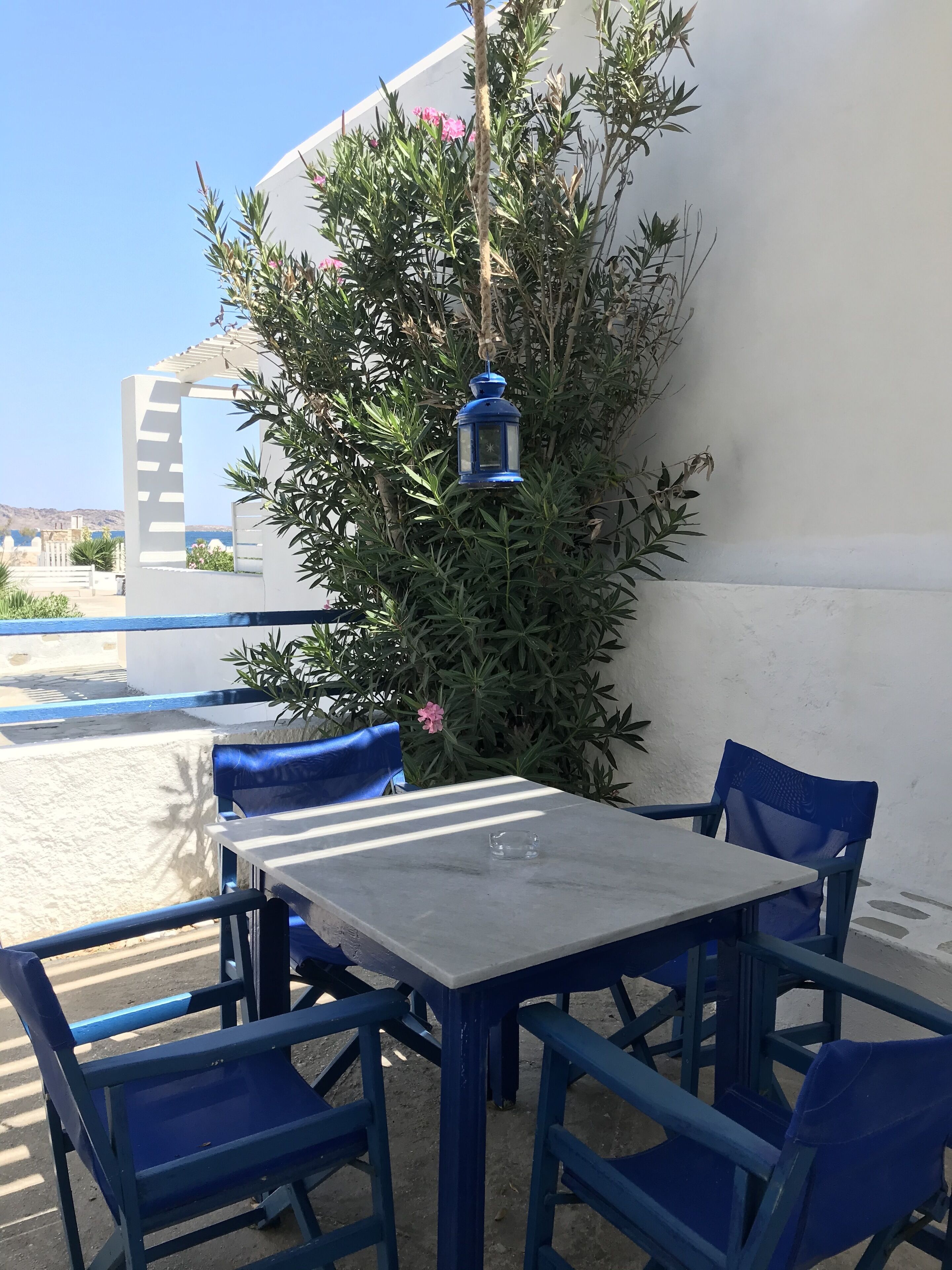 An outdoor seating area with a table and chairs, a hanging lantern, and a white wall with greenery.