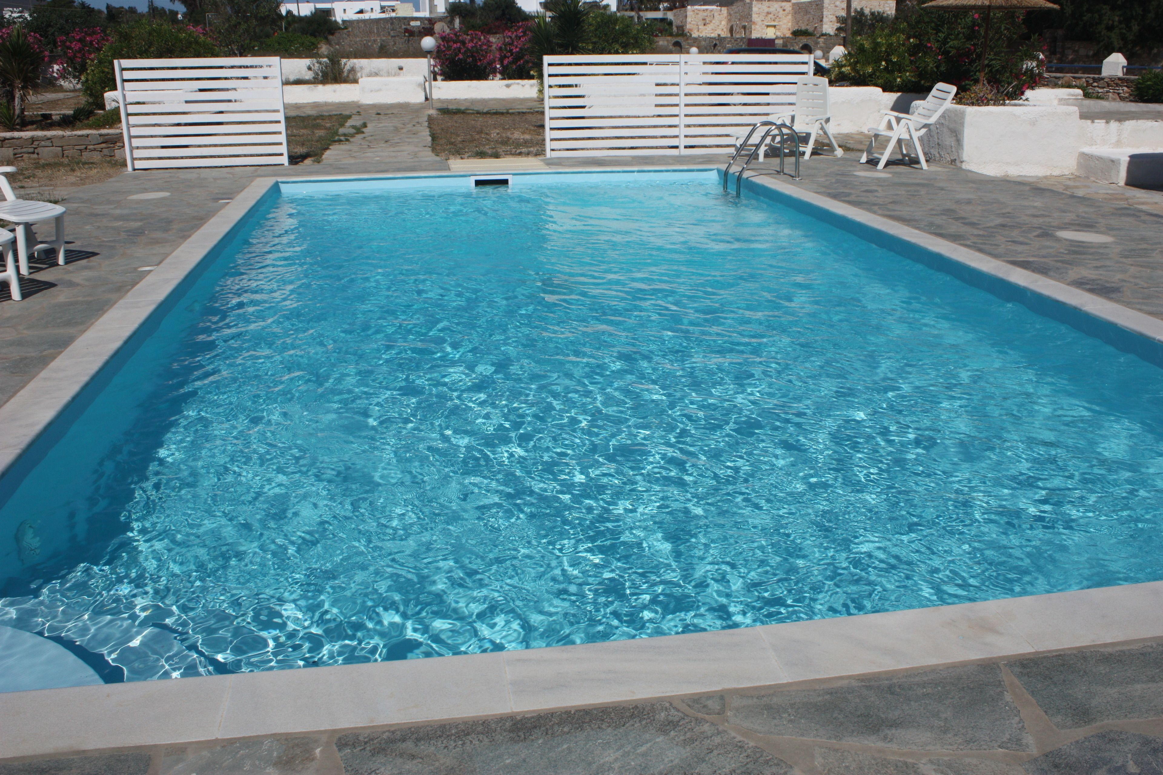 A rectangular swimming pool with clear blue water, surrounded by stone tiles and white lounge chairs.