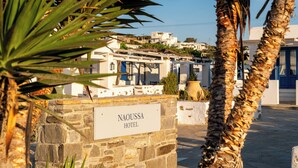 A stone wall with a sign reading "NAOUSSA HOTEL" and a view of white buildings in the background. - Naoussa Hotel Paros by Booking Kottas (Paros)