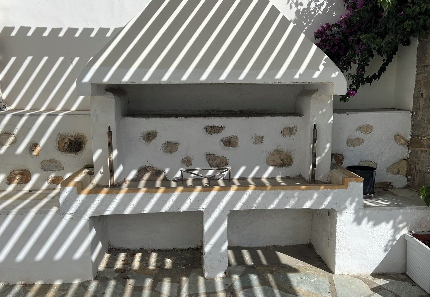 A stone-built outdoor seating area with a grill, surrounded by white walls with stone patches.