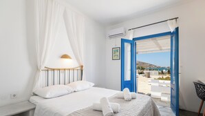 A bedroom with a bed, a bedside table, a lamp, and a view of the outside. - Naoussa Hotel Paros by Booking Kottas (Paros)