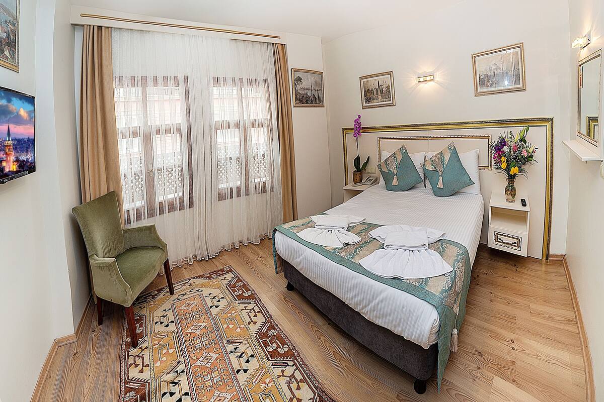 Une chambre à coucher bien rangée, avec un lit, une chaise, une table de chevet et un téléviseur fixé au mur.