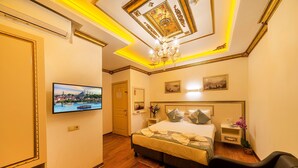 Ein Hotelzimmer mit einem großen Bett, einem an der Wand montierten Fernseher, einer Kandelaber und einem roten Teppich mit Muster.