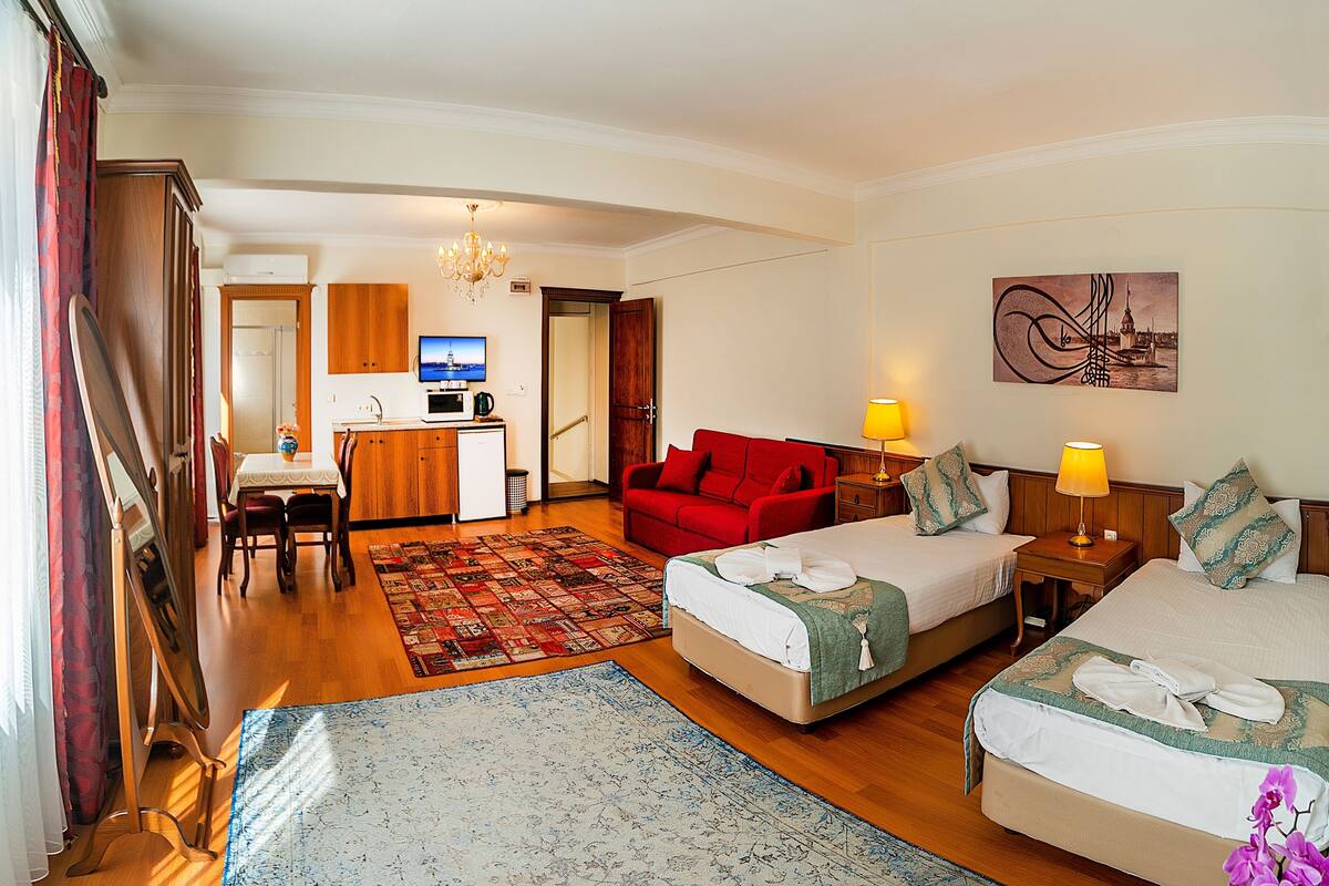 Une chambre d’hôtel avec un lit, un bureau équipé d’un ordinateur, un canapé rouge et un tableau accroché au mur.