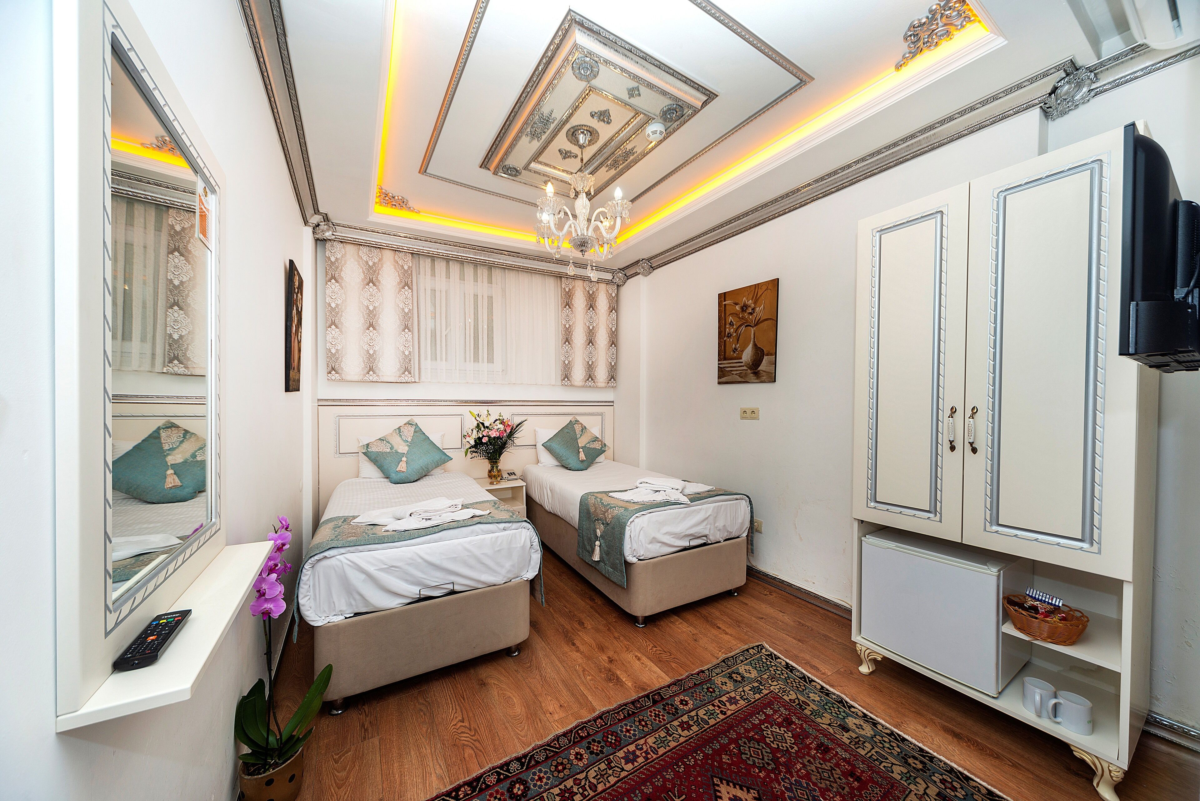 A bedroom with two beds, a large mirror, a chandelier, and a television.