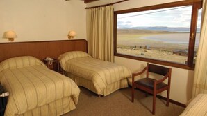 Une chambre d’hôtel avec deux lits, une chaise en bois, une table de chevet et une fenêtre donnant sur un paysage.
