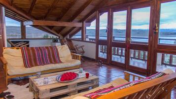 Une pièce chaleureuse avec un plafond en bois, de grandes fenêtres, un canapé, un banc en bois et une table basse rustique.