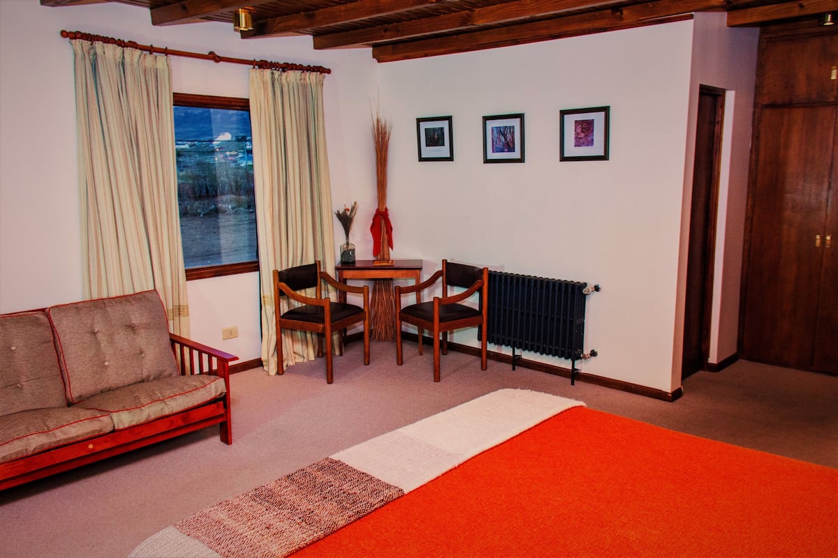 Habitación con sofá, dos sillones, una mesita, un radiador y tres cuadros en la pared.