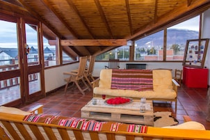 Un amplio balcón con mobiliario de madera, un sofá y una mesa con un plato decorativo y una copa.