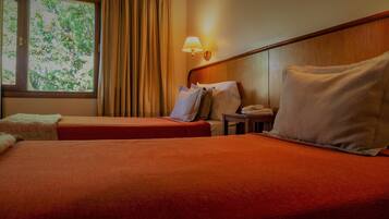 Una habitación de hotel con dos camas, una mesita de noche con lámpara y una ventana con cortinas.