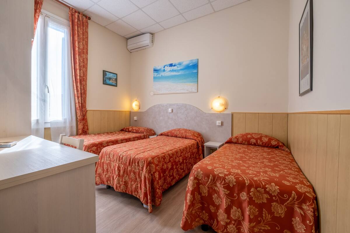 Habitación de hotel con tres camas, un escritorio y una ventana con cortinas.