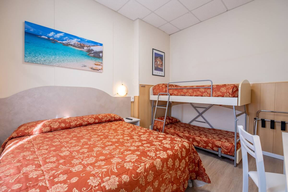 Una habitación con una cama litera, una cama individual, una mesita de noche, una lámpara y un cuadro de una playa.