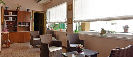 A room with wicker furniture, a tiled floor, and large windows with white blinds.