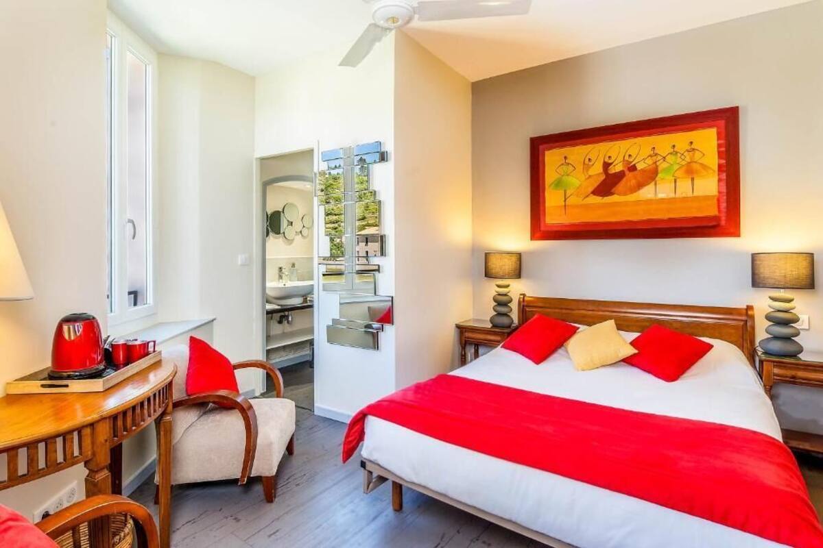 A hotel room with a bed, a desk, a chair, a window, and a painting on the wall.