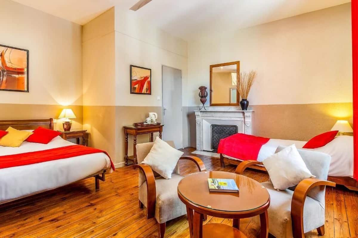 A hotel room with two beds, a fireplace, a mirror, and a small table.