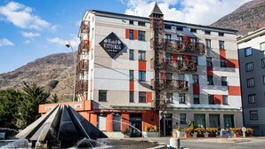 Un hotel con un letrero llamativo, una fuente de agua y montañas al fondo.