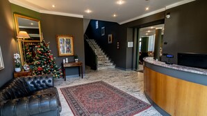 Vestíbulo de hotel con un árbol de Navidad, sofá de cuero, suelo de mármol, escalera y mostrador de recepción.
