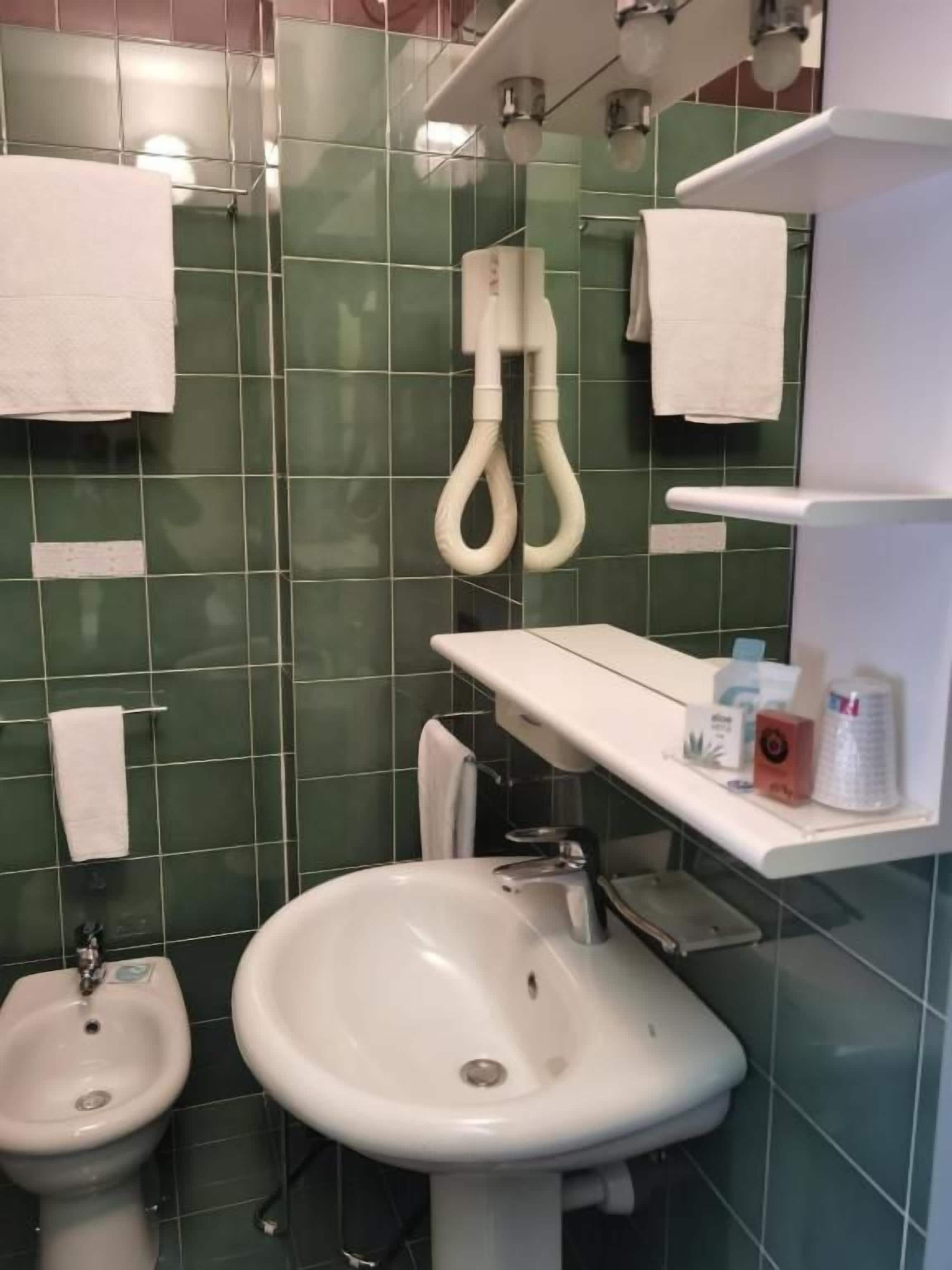 Un baño con azulejos verdes, un bidé, un lavabo y un toallero.