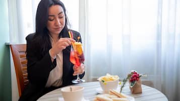 A person seated at a table with a drink, a bowl of chips, and a sandwich.