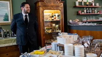 A man in a suit standing next to a wooden display cabinet filled with bottles, with a buffet table in the foreground.