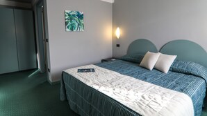 Una habitación de hotel con una cama, una mesita de noche, una lámpara de pared y un cuadro.