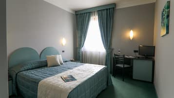 A hotel room with a bed, a desk, a chair, a TV, and a painting on the wall.