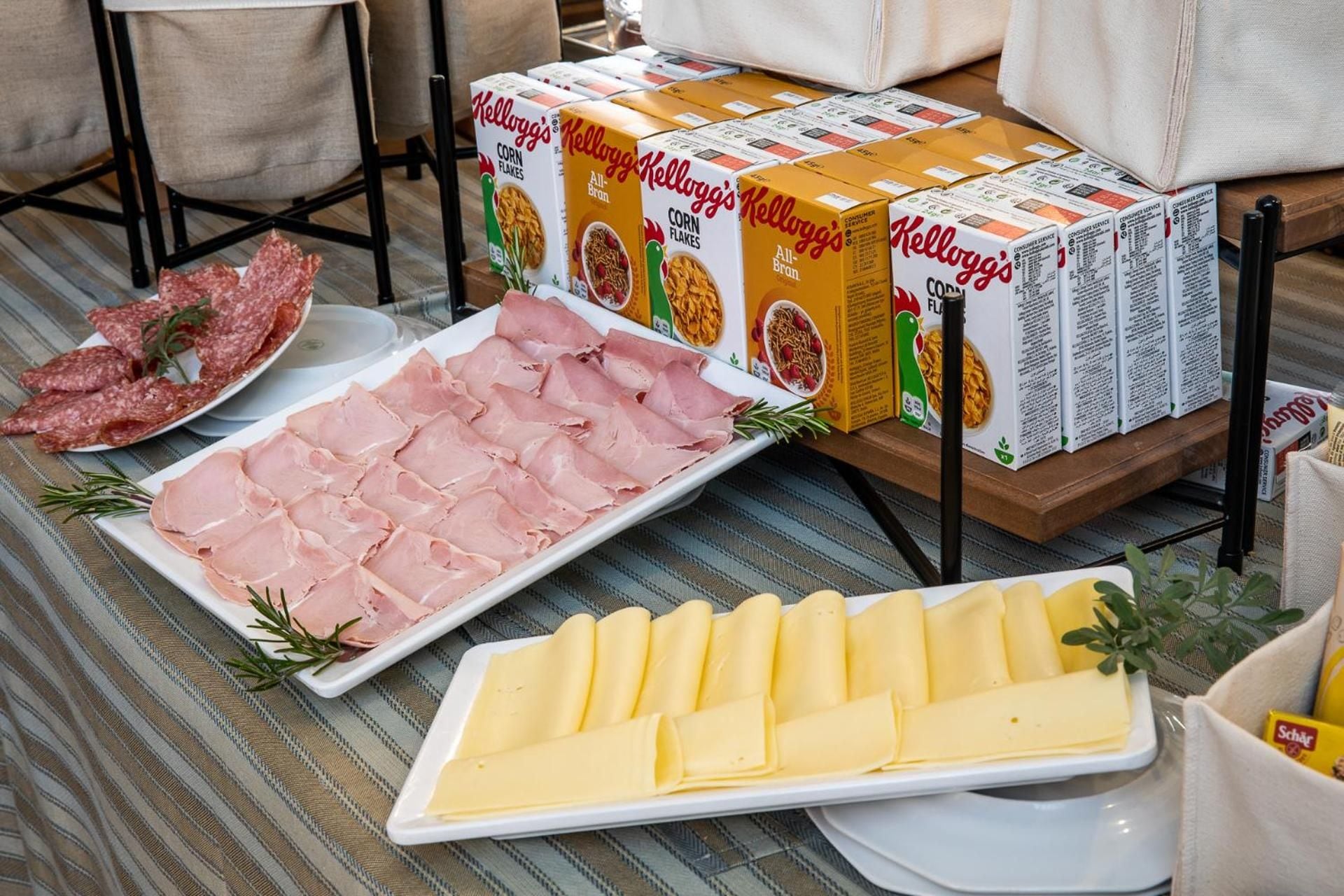 A buffet table with various food items including sliced ham, cheese, and cereal boxes.
