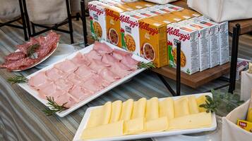 A buffet table with various food items including sliced ham, cheese, and cereal boxes.