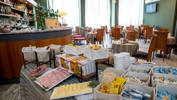 A hotel dining area with multiple tables, chairs, a bar with liquor bottles, and various food items displayed.