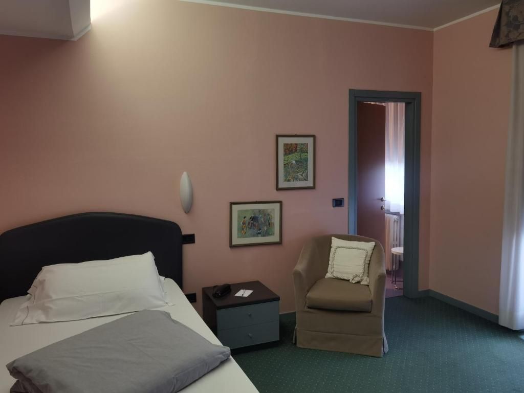 A hotel room with a bed, a chair, a nightstand, and two framed pictures on the wall.