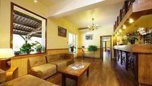 Amplia sala de estar con piso de madera, un sofá, una mesa de centro y una mesa de comedor. Hay una zona de cocina con barra y varias plantas.