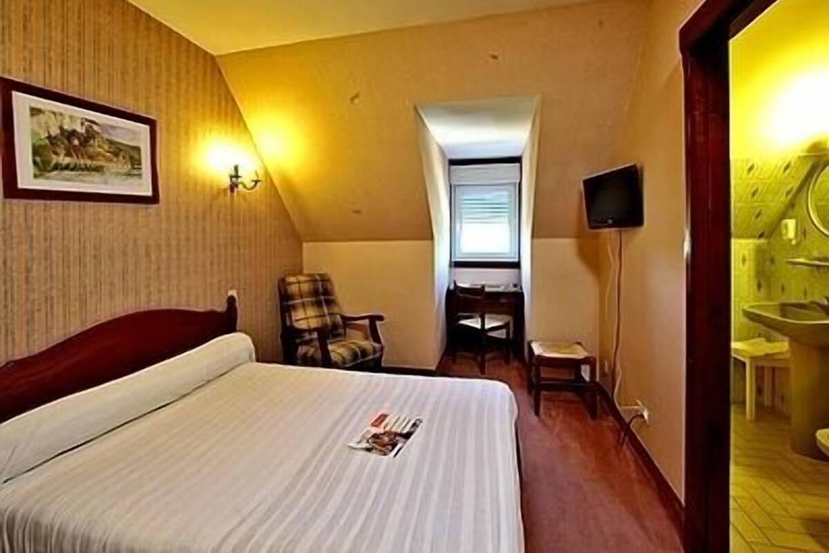 A hotel room with a bed, a chair, a desk, a television, and a bathroom visible through an open door.