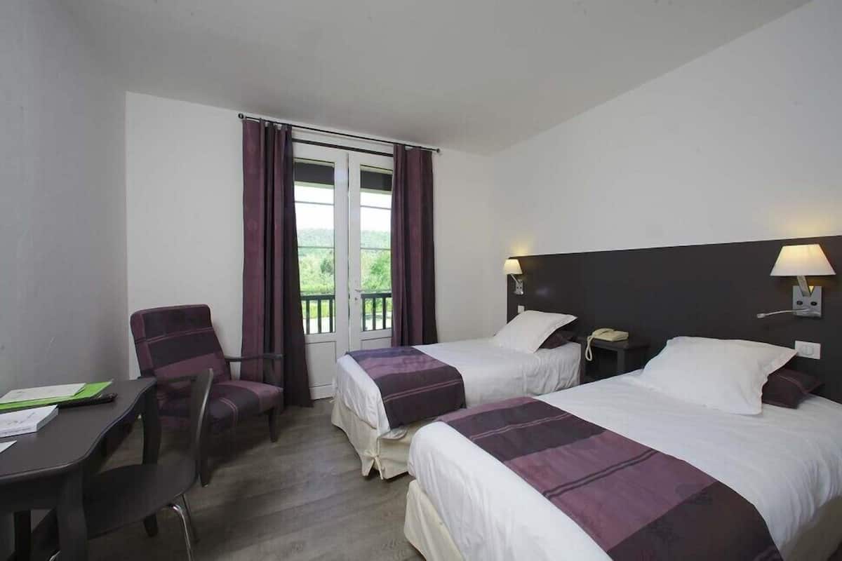 A hotel room with two beds, a desk, a chair, and a window with curtains.