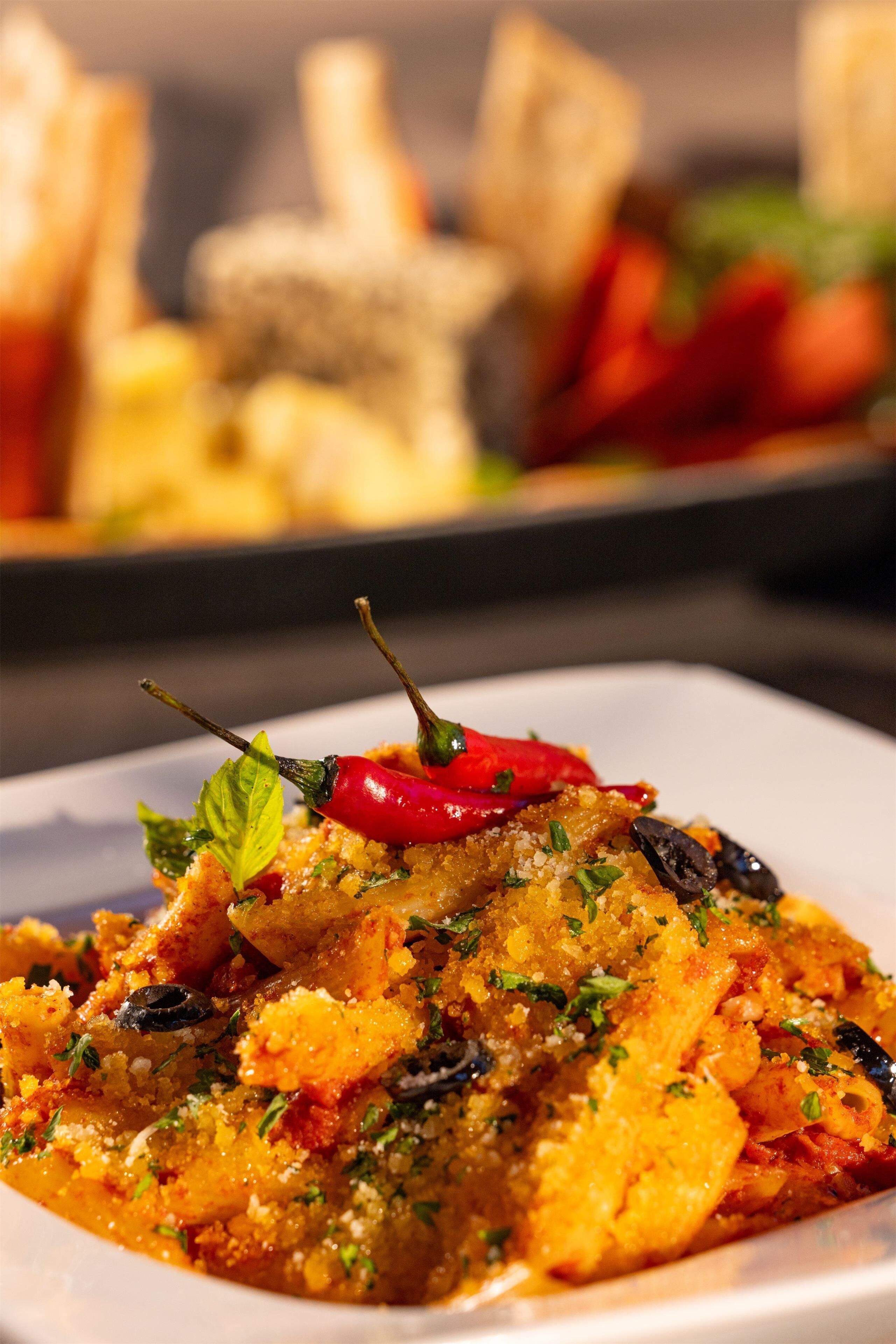 A close-up of a dish with pasta, herbs, and a red chili pepper on top.