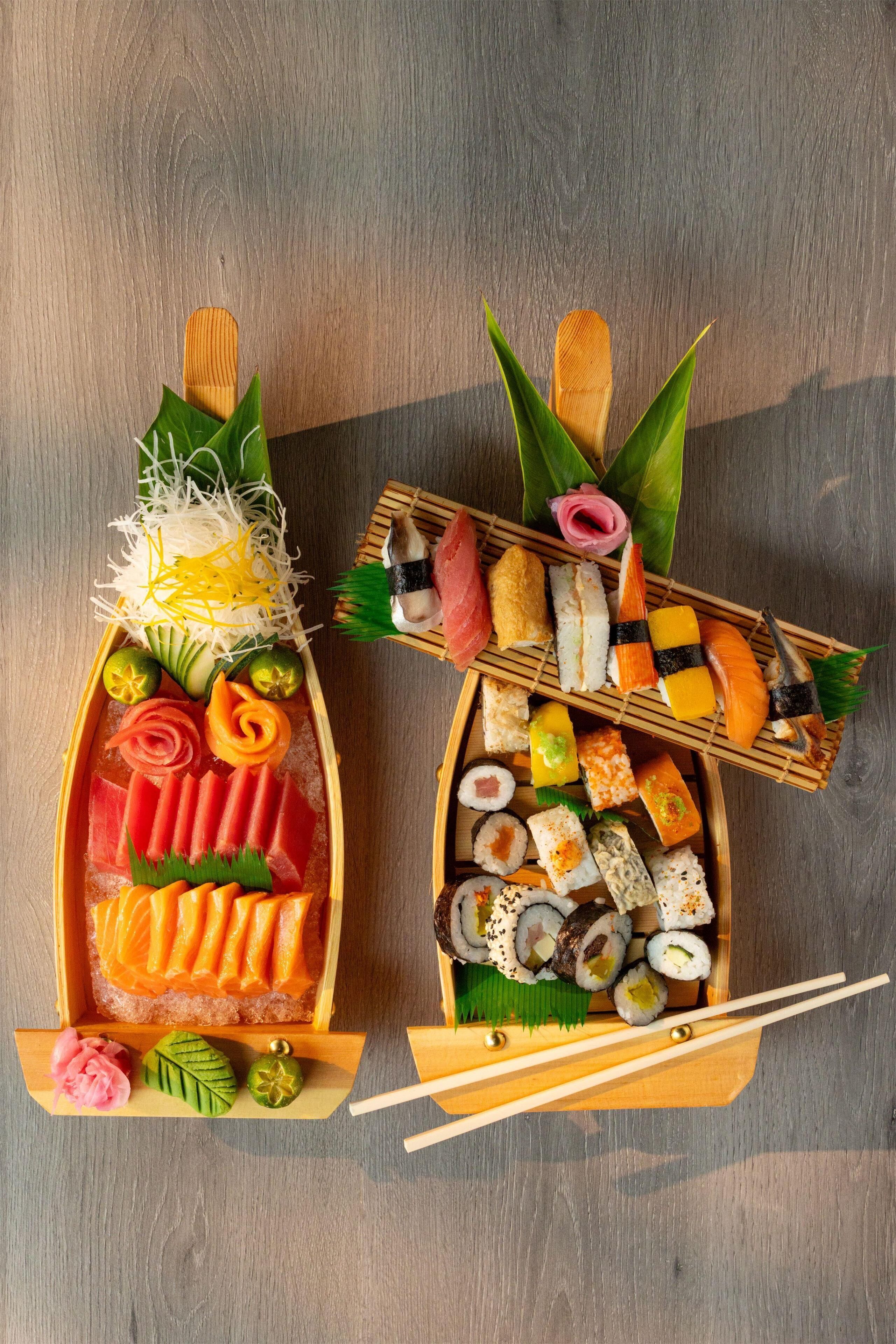 Two wooden sushi boats with various sushi pieces and garnishes on a wooden table.