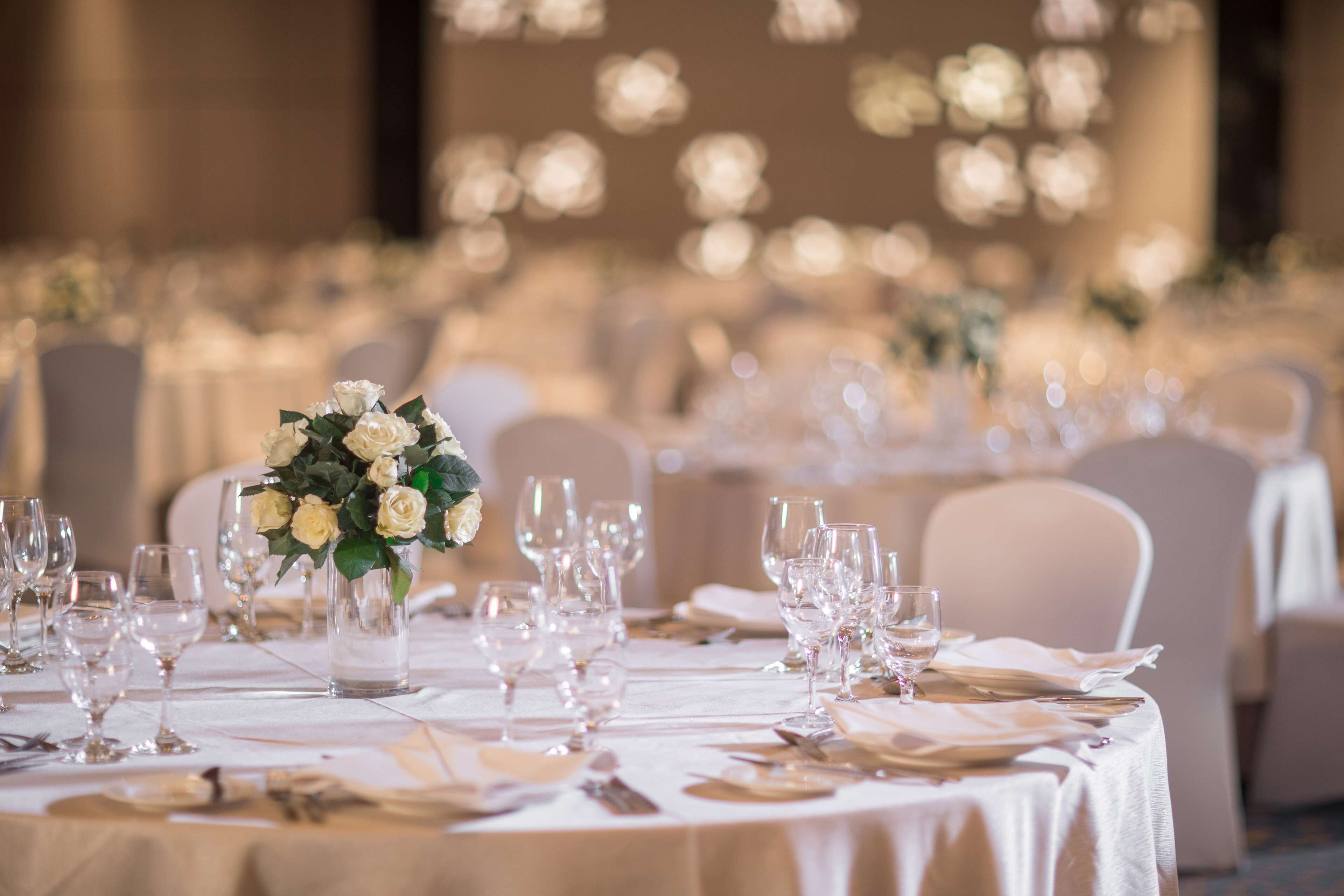 A banquet hall with round tables set for a formal event, featuring white tablecloths and floral centerpieces.