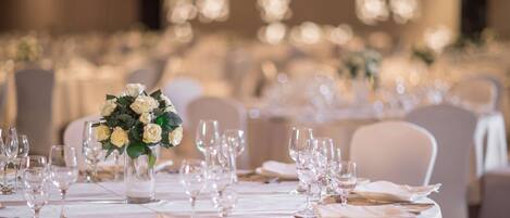 A banquet hall with round tables set for a formal event, featuring white tablecloths and floral centerpieces.