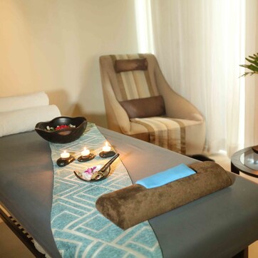A massage table with candles, a chair, and a small table with a plant and bowls of flowers.