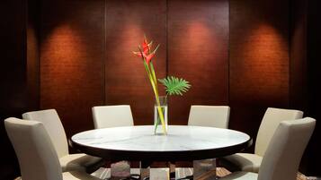 A round table with a marble top surrounded by six upholstered chairs. A tall vase with a single plant is placed on the table.
