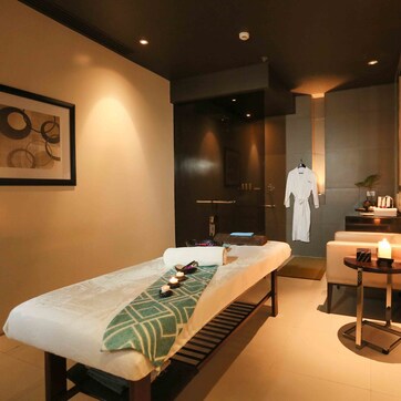 A modern spa room with a massage table, a small table with candles, and a robe hanging on a rack.