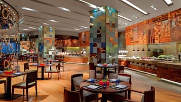 Un restaurante moderno con suelo de madera, mesas redondas y sillas. Se observan pilares decorativos y una pared con un diseño geométrico.